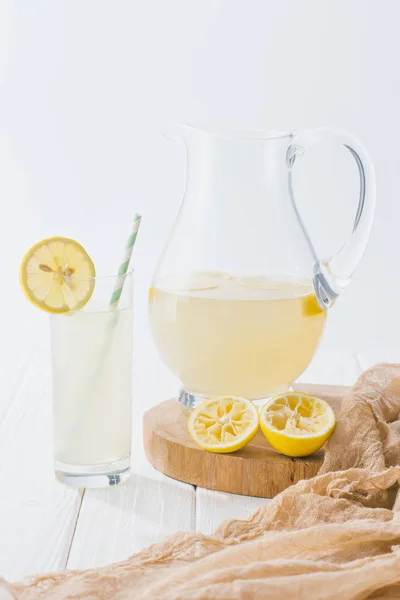 Nahaufnahme von Limonade im Glas mit Stroh und Krug auf weißer Holzoberfläche vor grauem Hintergrund — Stockfoto