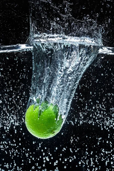 Close up view of fresh lime in water with splashes isolated on black — Stock Photo