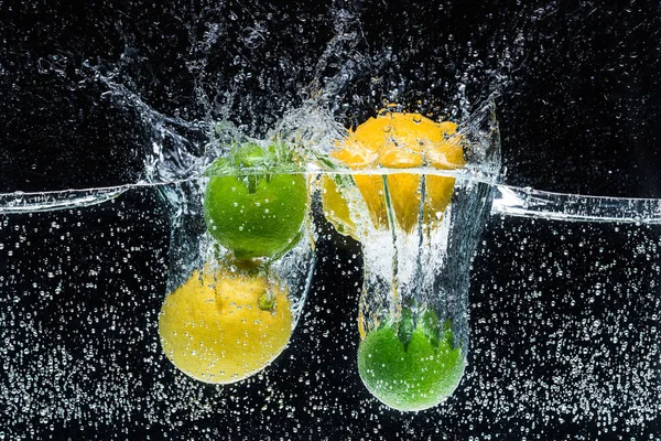 Vue rapprochée des citrons frais et des citrons verts dans l'eau isolée sur noir — Photo de stock