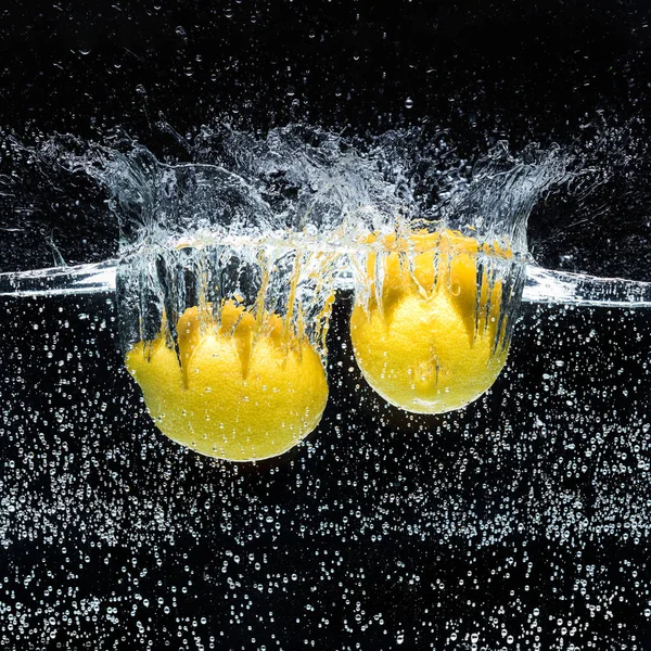 Vista de cerca de limones en agua aislada en negro - foto de stock