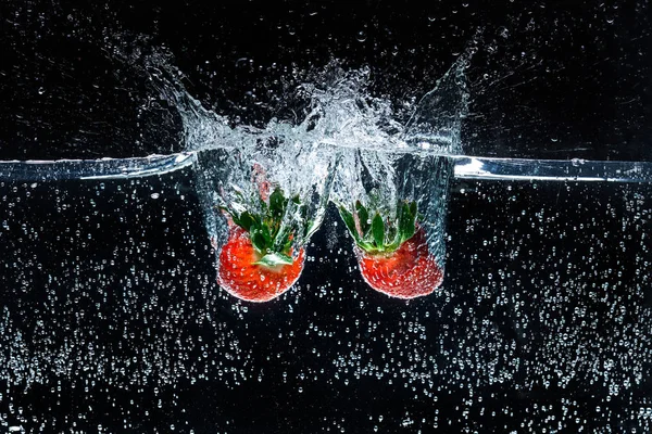 Vista de cerca del movimiento de fresas maduras que caen en el agua aisladas en negro - foto de stock