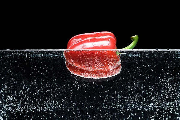 Vista de cerca del pimiento rojo maduro en agua aislada en negro — Stock Photo