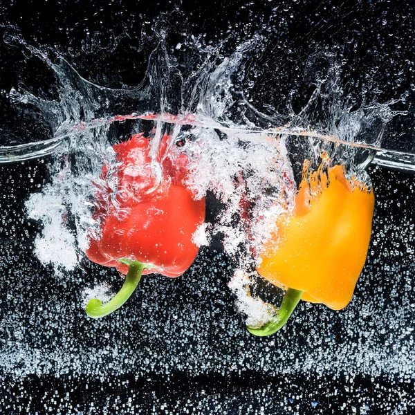 Vista de cerca de pimientos rojos y amarillos en agua aislada en negro - foto de stock