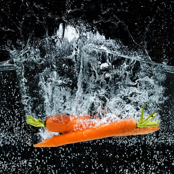 Vue rapprochée des carottes dans l'eau isolée sur noir — Photo de stock