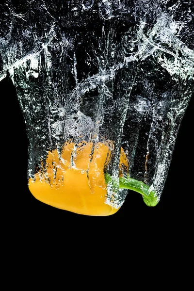 Vue rapprochée du mouvement du poivron jaune tombant dans l'eau isolée sur noir — Photo de stock