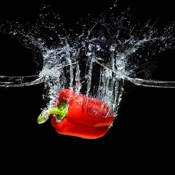 Nahaufnahme der Bewegung von rotem Paprika, der isoliert auf schwarz ins Wasser fällt — Stockfoto