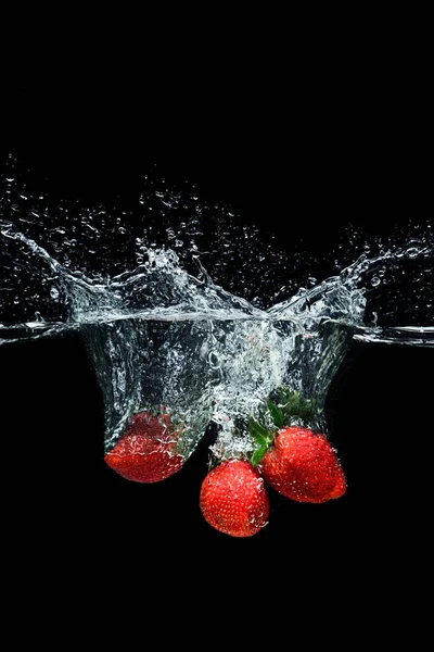 Vue rapprochée du mouvement des fraises mûres tombant dans l'eau isolée sur noir — Photo de stock