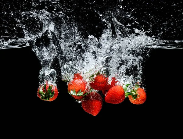 Vue rapprochée du mouvement des fraises mûres tombant dans l'eau isolée sur noir — Photo de stock