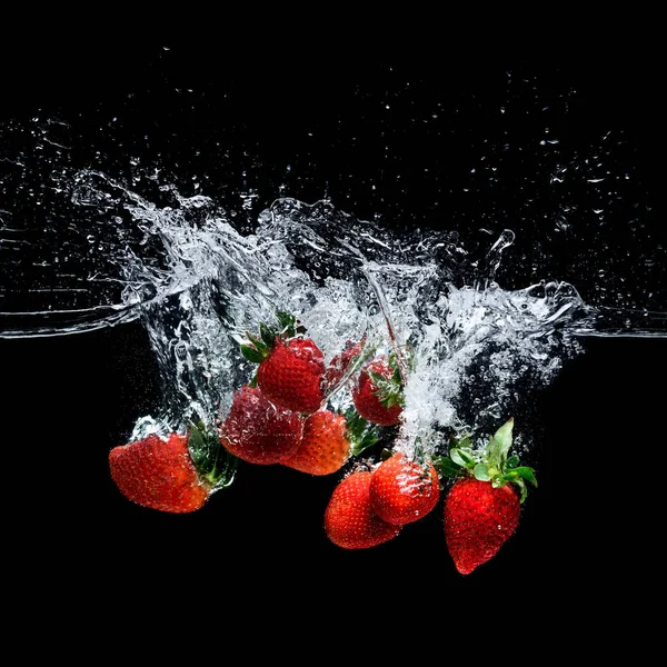 Nahaufnahme der Bewegung reifer Erdbeeren, die isoliert auf schwarz ins Wasser fallen — Stockfoto