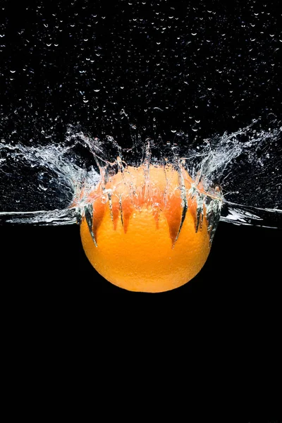 Крупним планом вид свіжих апельсинових цитрусових, що падають у воду ізольовані на чорному — стокове фото