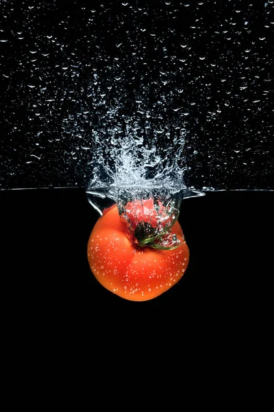 Nahaufnahme von Tomaten, die ins Wasser fallen, mit Spritzern isoliert auf schwarz — Stockfoto