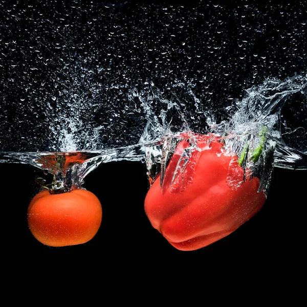 Vue rapprochée du poivron et de la tomate tombant dans l'eau isolée sur noir — Photo de stock