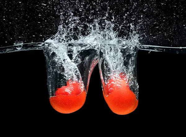 Вблизи вид спелых помидоров, падающих в воду изолированных на черном — стоковое фото