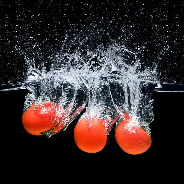 Vue rapprochée des tomates mûres tombant dans l'eau isolée sur noir — Photo de stock