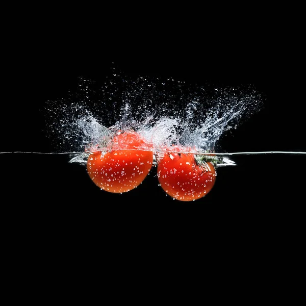 Vista de perto de tomates maduros caindo em água isolada em preto — Fotografia de Stock