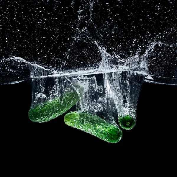 Nahaufnahme von reifen Gurken, die mit Spritzern isoliert auf schwarz ins Wasser fallen — Stockfoto