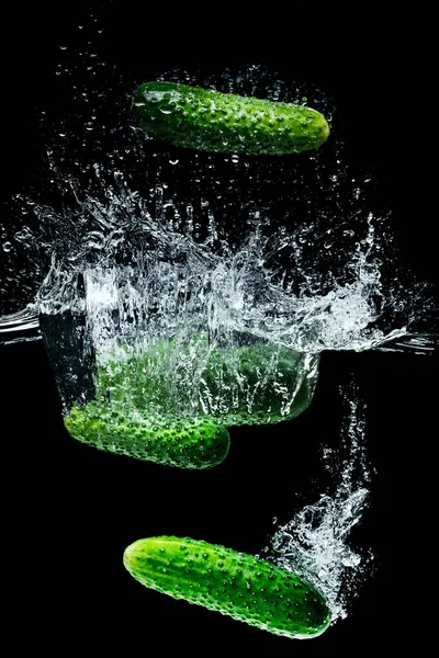 Close up view of ripe cucumbers falling into water with splashes isolated on black — Stock Photo