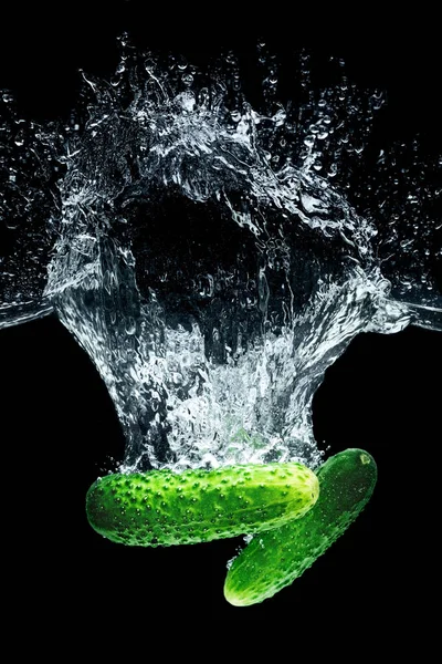 Close up view of ripe cucumbers falling into water with splashes isolated on black — Stock Photo