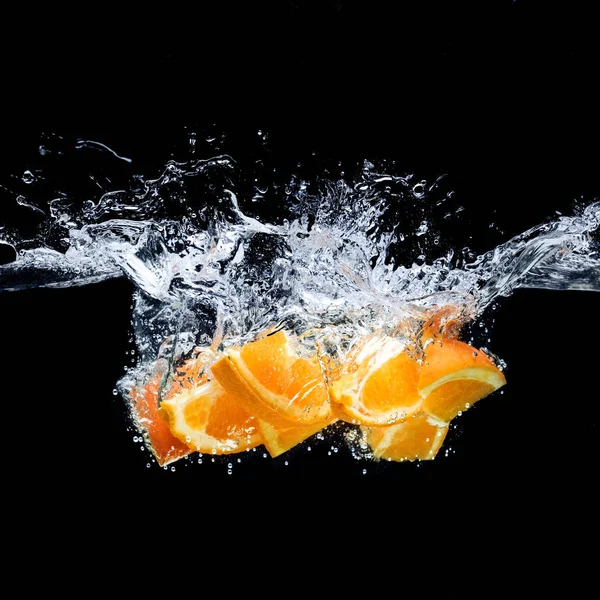 Vista de perto de pedaços de frutas cítricas laranja em água isolada em preto — Fotografia de Stock