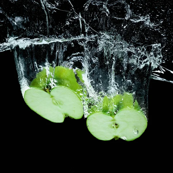 Nahaufnahme von grünen Apfelstücken im Wasser isoliert auf schwarz — Stockfoto