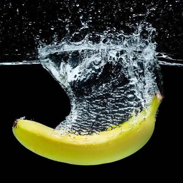 Close up view of banana in water with splashes isolated on black — Stock Photo