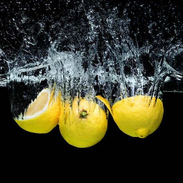 Vista ravvicinata di limoni freschi in acqua con spruzzi isolati su nero — Foto stock