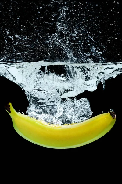 Vue rapprochée de la banane dans l'eau avec éclaboussures isolées sur noir — Photo de stock