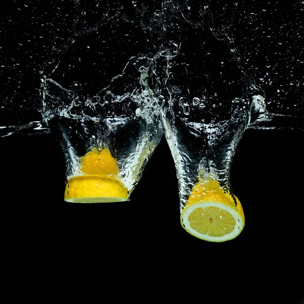 Close up view of fresh lemon pieces in water with splashes isolated on black — Stock Photo