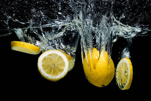 Vista ravvicinata di pezzi di limone fresco in acqua con spruzzi isolati su nero — Foto stock