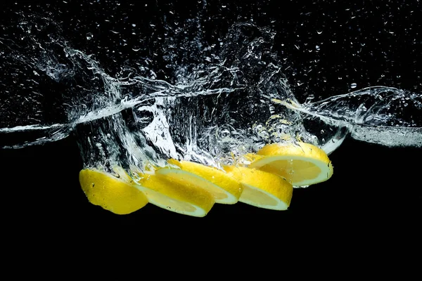 Vista ravvicinata di pezzi di limone fresco in acqua con spruzzi isolati su nero — Foto stock