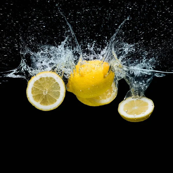 Vista ravvicinata di pezzi di limone fresco in acqua con spruzzi isolati su nero — Foto stock