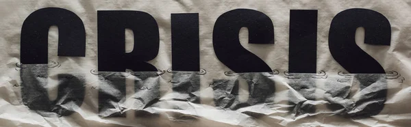 Panoramic shot of black word crisis sinking in paper symbolizing water on grey paper background — Stock Photo