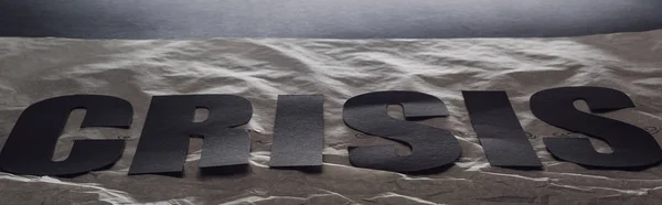 Panoramic shot of black word crisis on paper symbolizing water on black background with lighting — Stock Photo