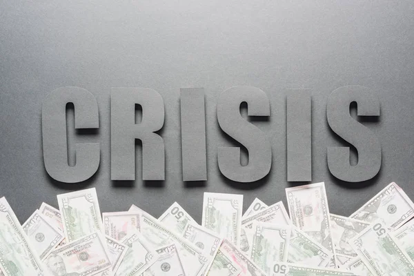 Top view of word crisis near scattered dollar banknotes on grey background with shadows — Stock Photo