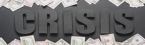 Top view of word crisis near scattered dollar banknotes on black background with shadows, panoramic shot — Stock Photo