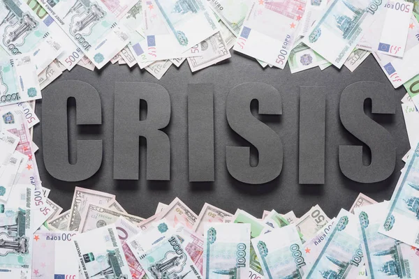Vista superior de la palabra crisis en el marco del dólar y los billetes en euros sobre fondo negro con sombras - foto de stock