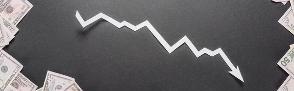 Tiro panorámico de flecha blanca de recesión cerca de billetes de dólar sobre fondo negro - foto de stock