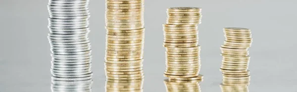 Панорамный снимок сложенных серебряных и золотых монет на поверхности с отражением, изолированным на сером — стоковое фото