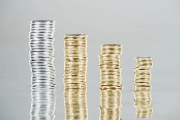 Stacks of silver and golden coins on surface with reflection isolated on grey — Stock Photo