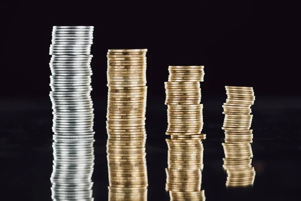 Stacks of silver and golden coins on surface with reflection isolated on black — Stock Photo