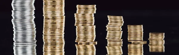 Panoramic shot of stacked silver and golden coins on surface with reflection isolated on black — Stock Photo