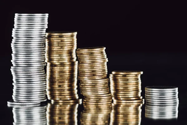 Stacks of silver and golden coins on surface with reflection isolated on black — Stock Photo