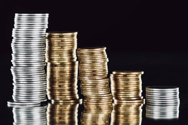 Pilas de plata y monedas de oro en la superficie con reflejo aislado en negro — Stock Photo