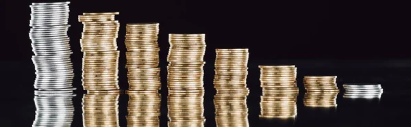 Panoramic shot of stacked silver and golden coins on surface with reflection isolated on black — Stock Photo
