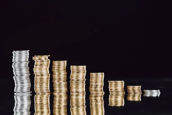 Stacks of silver and golden coins on surface with reflection isolated on black — Stock Photo