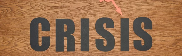 Draufsicht auf schwarzes Papier geschnittenes Wort Krise auf Holzschreibtisch, Panoramaaufnahme — Stockfoto