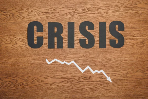 Vista dall'alto di carta nera taglio parola crisi e recessione freccia sulla scrivania di legno — Foto stock