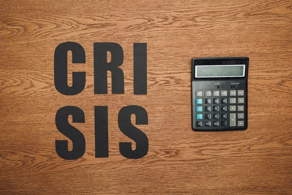 Верхний вид черной бумаги сократить кризис слова рядом с калькулятором на деревянном столе — стоковое фото