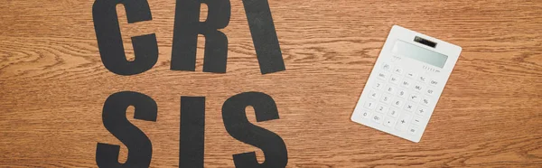 Draufsicht auf schwarzes Papier geschnittenes Wort Krise nahe weißem Taschenrechner auf Holzschreibtisch, Panoramaaufnahme — Stockfoto