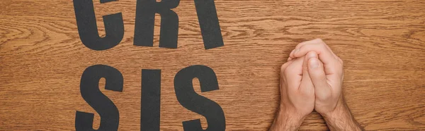 Cropped view of male folded hands near black paper cut word crisis on wooden desk, panoramic shot — Stock Photo